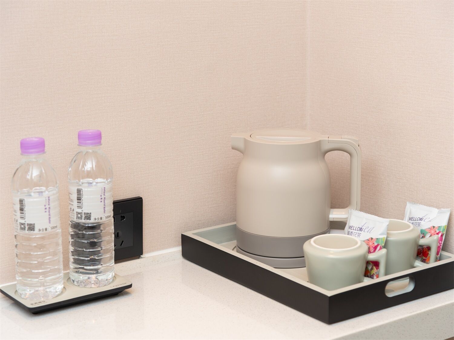 A tray with a kettle, two water bottles, a mug, and tea packets.