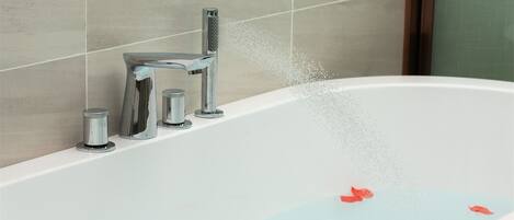 A bathtub with water flowing from a modern faucet, a small container, and a single red flower floating in the water.
