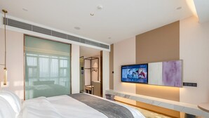 Une chambre d’hôtel moderne dotée d’un grand lit, d’une télévision et d’une cloison en verre.