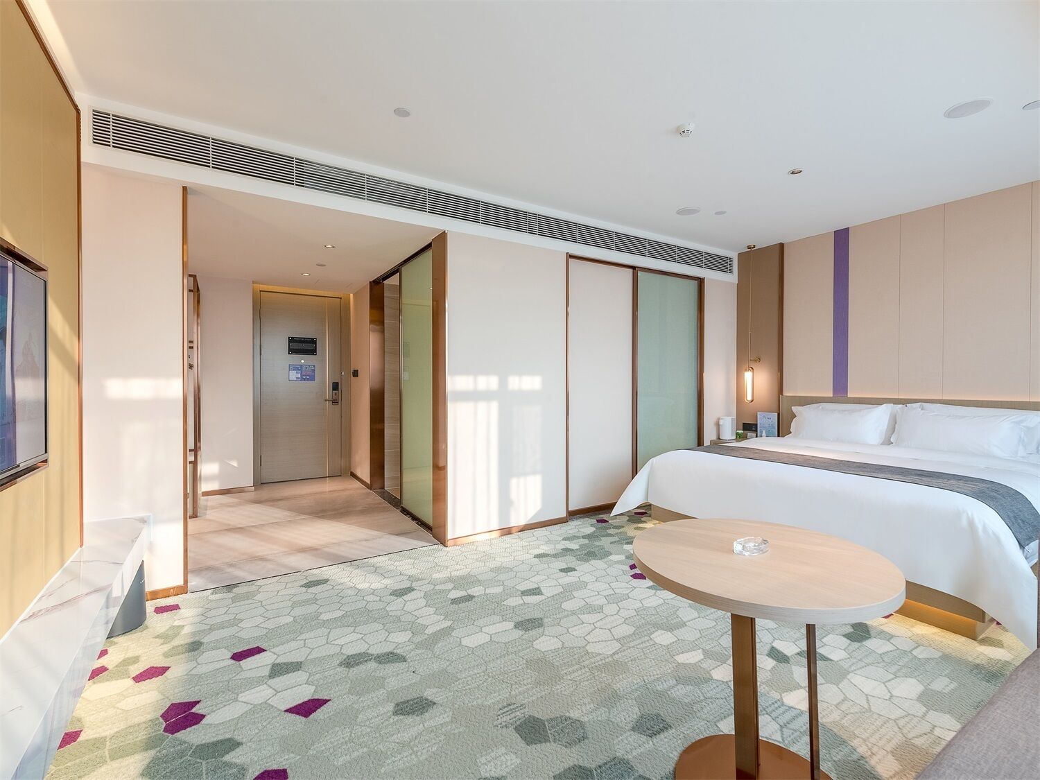 A hotel room with a bed, a small round table, a walk-in closet, and a door leading to another room.