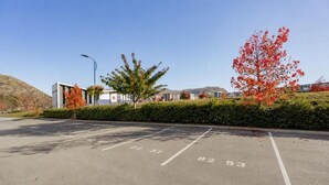 A parking lot with marked spaces, a building in the background, and autumn foliage. - Après Ski Apartment with Full Kitchen and Carpark (Queenstown)