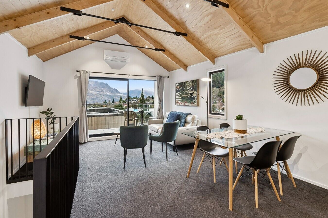A modern interior with a dining area, a sofa, a TV, and a view of mountains.