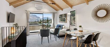 A modern interior with a dining area, a sofa, a TV, and a view of mountains.