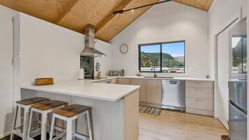 A modern kitchen with a large island, bar stools, stainless steel appliances, and a view of the outdoors.