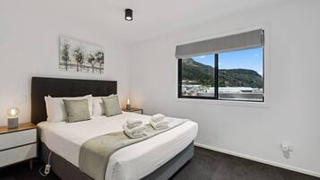 A bedroom with a bed, nightstands, a bedside lamp, a window with a view, and a ceiling light.