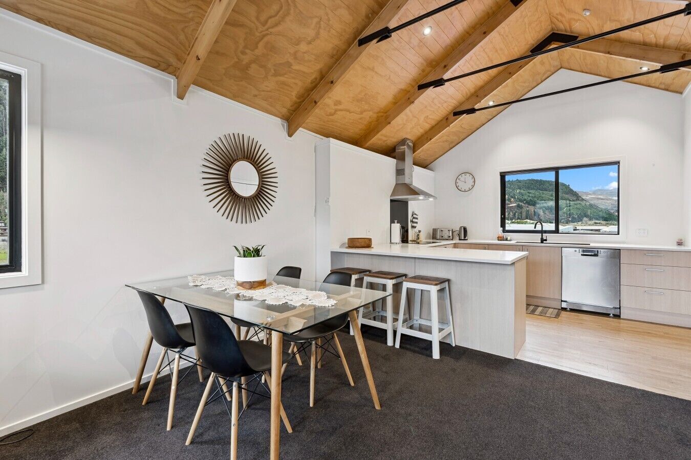 A modern kitchen with a wooden ceiling, a dining area with a glass table, and a view of the outdoors.