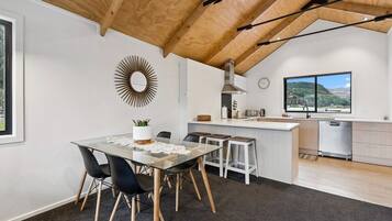 A modern kitchen with a wooden ceiling, a dining area with a glass table, and a view of the outdoors.