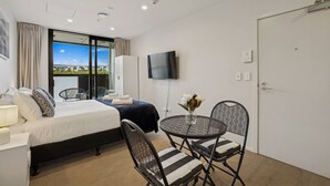 Una camera d'albergo con un letto, una televisione, un tavolo da pranzo con sedie, una finestra con tende e una porta.