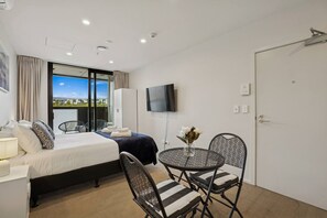 Une chambre d’hôtel comprenant un lit, une télévision, une table à manger avec des chaises et une vue sur l’extérieur grâce à une grande fenêtre.
