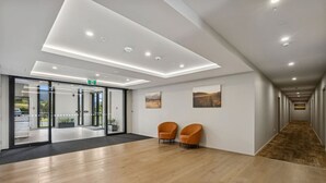 Una hall moderna con pavimento in legno, porte in vetro che danno sull'esterno e due poltrone arancioni.