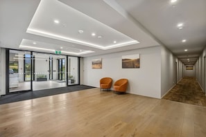 Un hall d’entrée moderne avec un plancher en bois, des portes vitrées donnant sur l’extérieur, deux fauteuils orange et un couloir également doté d’un plancher en bois.