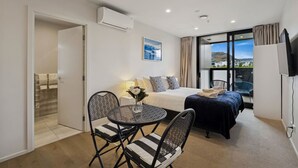 Camera d'albergo moderna con un letto, un tavolo da pranzo, sedie, una TV e un'ampia finestra vista.