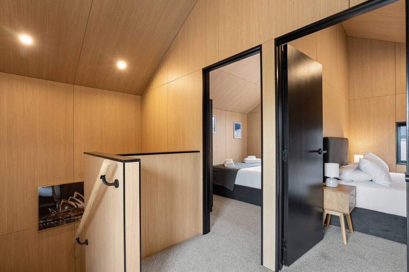 A modern hotel room with a wooden interior, a bed, a bedside table, and a small seating area.