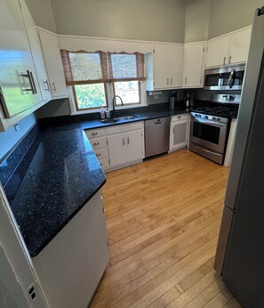 A kitchen with white cabinets, a black countertop, a stove, and a dishwasher.