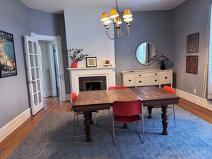 A dining area with a wooden table, red chairs, a white fireplace, and a chandelier.