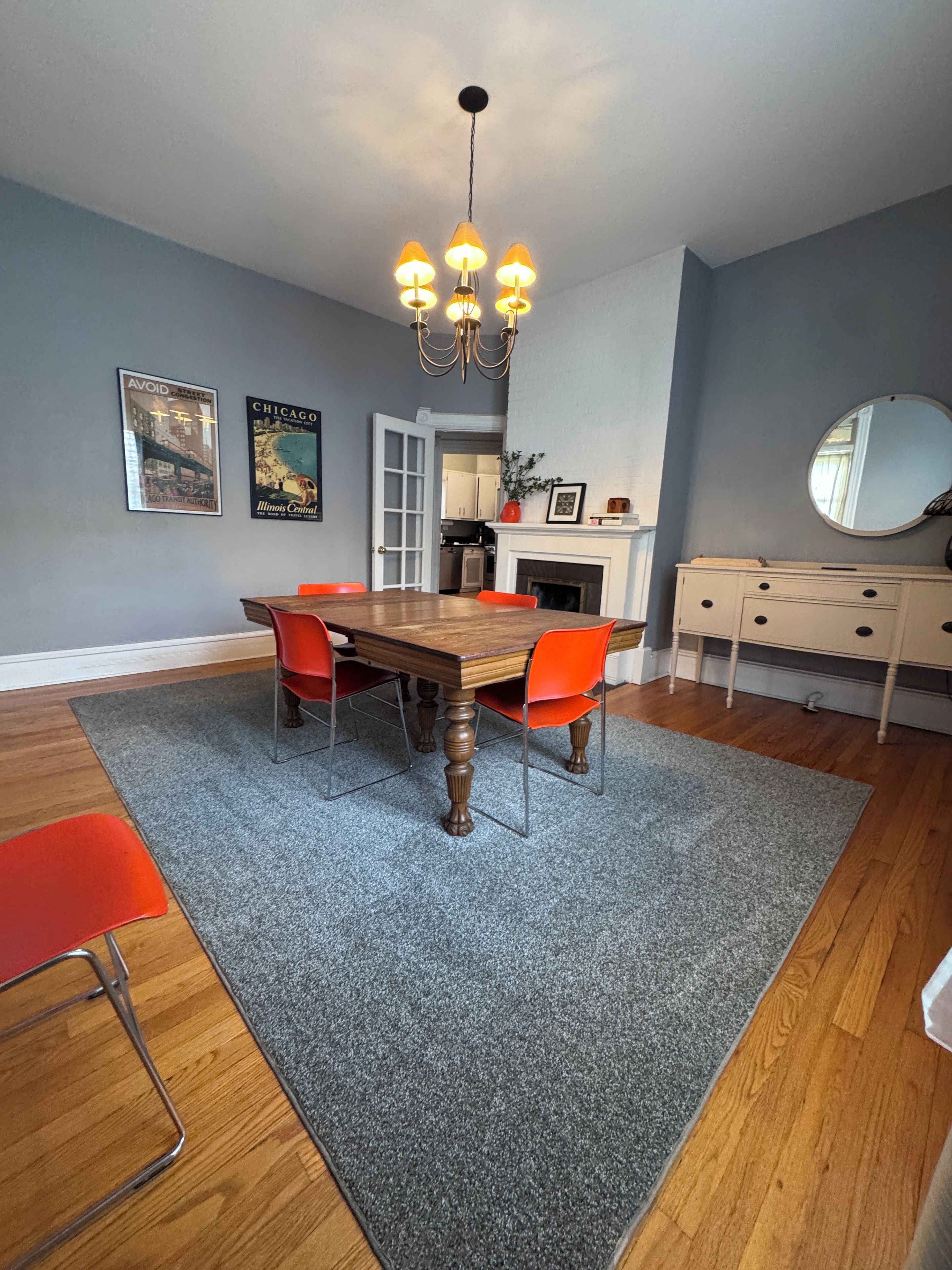 A dining area with a wooden table, red chairs, a chandelier, and a gray carpet.