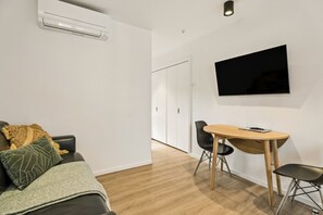 Un espace de vie moderne comprenant un canapé, une table à manger avec des chaises, un téléviseur à écran plat fixé au mur et un appareil de climatisation.