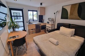 Ein kompaktes Hotelzimmer mit Bett, Schreibtisch, Küchenzeile und großem Fenster.