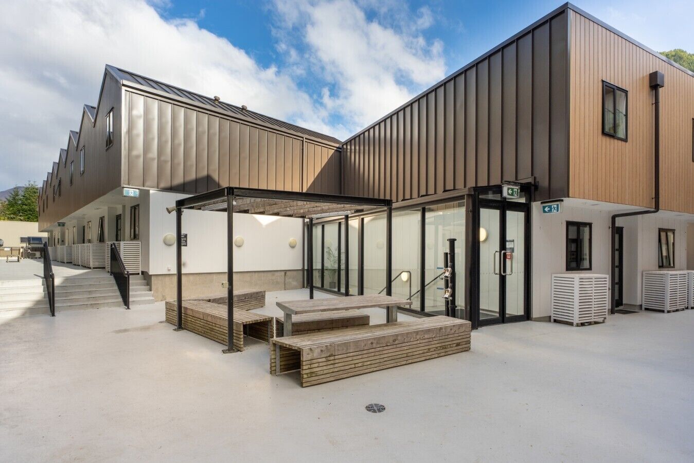 A modern building with a covered outdoor seating area, a staircase, and a glass entrance.