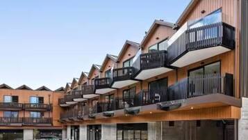 A modern multi-story building with balconies, a parking area, and a clear sky.