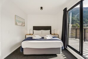 A hotel room with a bed, two bedside tables, a painting on the wall, and a large window with a view of the outdoors.