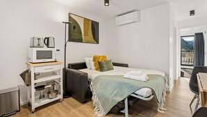 Ein kleines Hotelzimmer mit Bett, Küchenzeile, Tisch und Blick auf einen Balkon.