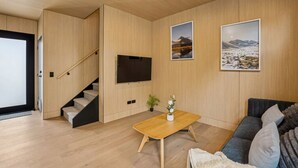 Moderni olohuone, jossa on puulattia, portaikko, litteänäyttöinen televisio, sohvapöytä ja sohva.