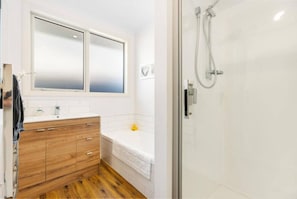 A bathroom with a wooden vanity, a white bathtub, and a glass shower enclosure. - Best for Mates! Double Ensuite Home! (Cromwell)