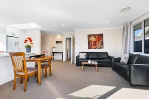 A modern living room with a sofa, coffee table, and dining area with chairs and a table. - Best for Mates! Double Ensuite Home! (Cromwell)