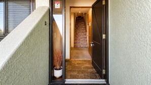 Une entrée d’immeuble avec un panneau indiquant la présence d’un système de sécurité, un pot de fleurs, un escalier et une porte.