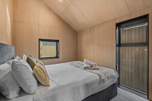 Een slaapkamer met een bed, kussens, een raam en een schuifdeur.