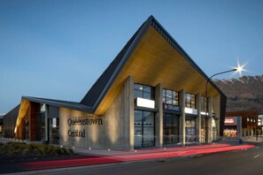 Een modern gebouw met een opvallend 'Queenstown Central'-bord, grote ramen en een berg op de achtergrond.