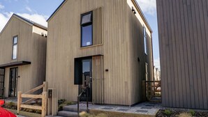 Una casa moderna de madera con un ventanal grande, una puerta visible y una escalera que lleva a la entrada.