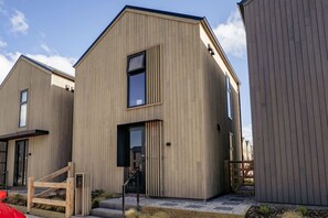 Ein modernes Holzhaus mit großem Fenster, einer sichtbaren Tür und einer Treppe zum Eingang.