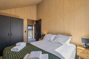 Een moderne hotelkamer met een groot bed, een donkerhouten garderobe en uitzicht door een geopende deur.