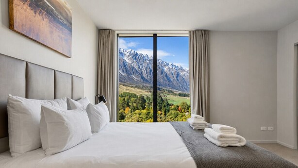 Habitación de hotel con una cama grande, vistas a las montañas y una ventana con cortinas.