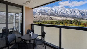 Un balcón con una mesa y sillas, una botella de vino y vistas a montañas nevadas.