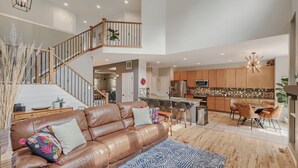 A spacious living area with a leather sofa, a staircase, a kitchen with wooden cabinets, and a dining area. - Comfy 4-Bedroom House in Castle Rock with Priv. Fenced-in Backyard/Dog Friendly. (Castle Rock)