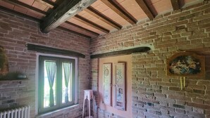 A room with exposed wooden beams, brick walls, a window with curtains, and a wall-mounted clock. - Lovely home in Sarnano with swimming pool (Sarnano)