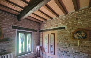 Ein Zimmer mit freiliegenden Holzbalken, Backsteinwänden, einem fenster mit Vorhängen und einer an der Wand befestigten Uhr.