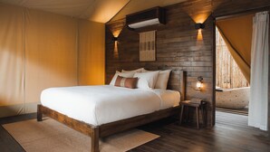 A bedroom with a wooden bed frame, a bedside table, a wall-mounted light, and a window with curtains.