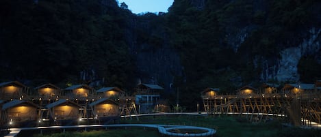 Un ensemble de chalets en bois disposés autour d’une structure centrale circulaire, le tout étant niché dans un paysage montagneux naturel.