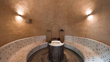 Sauna circular de paredes de piedra con un banco de madera y una estructura central de madera, posiblemente un asiento o calentador.