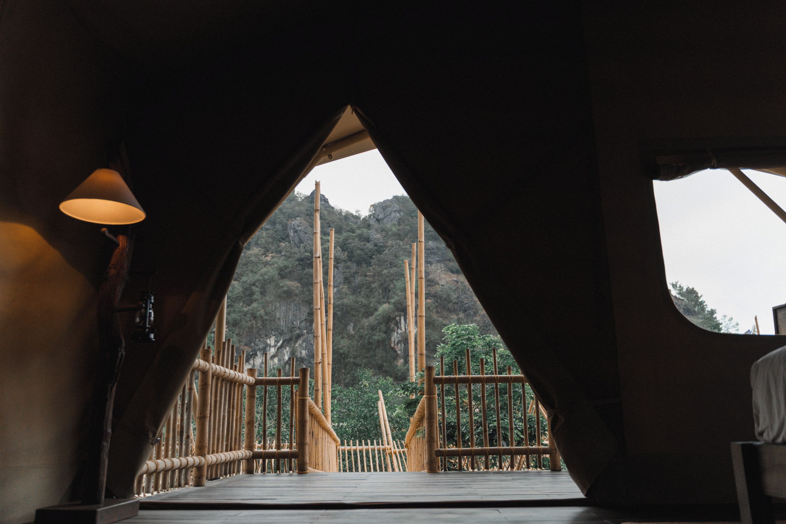 Una habitación con un ventanal grande, suelo de madera y vistas a construcciones de bambú.