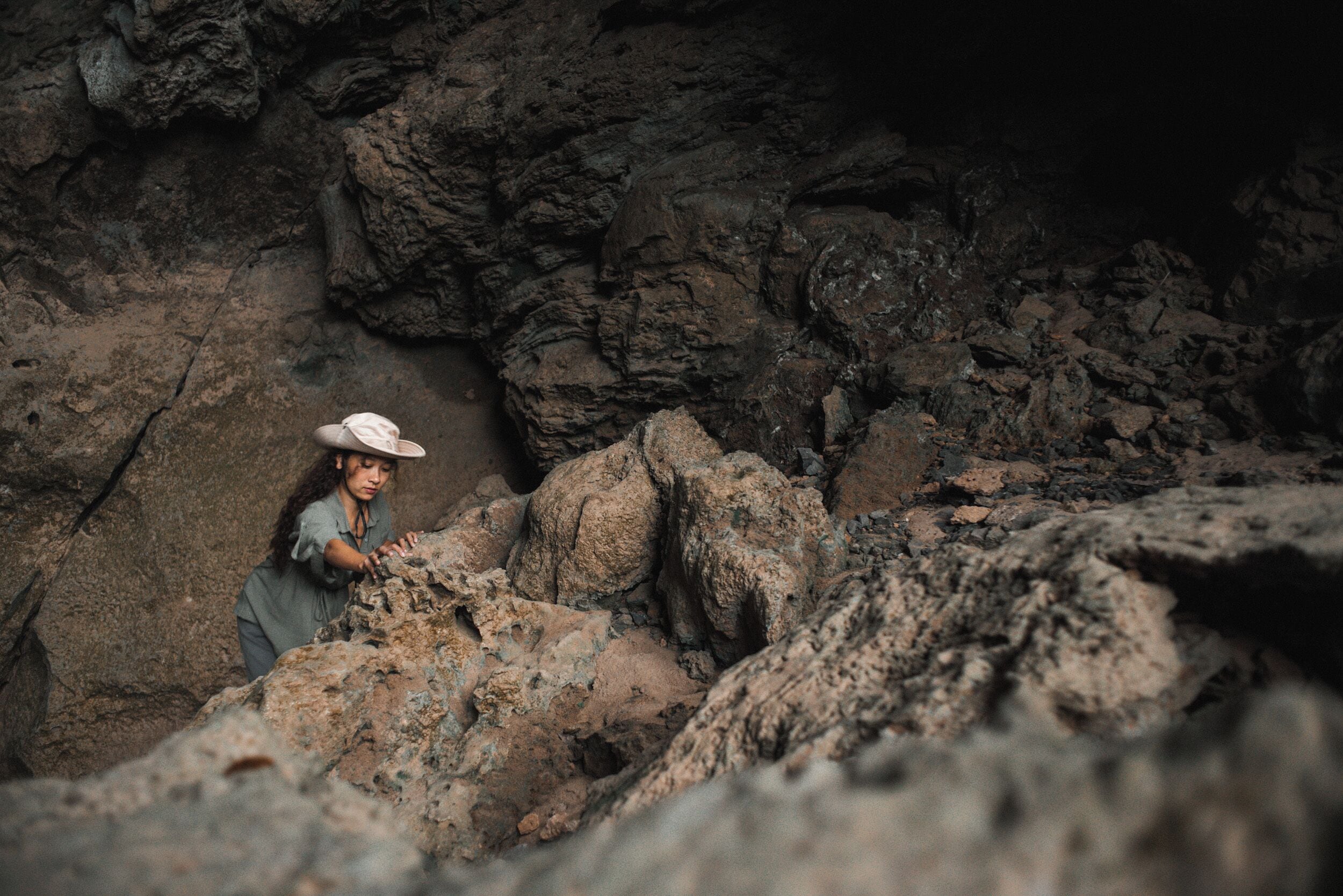 A person in a hat and long-sleeve shirt climbing rocks.
