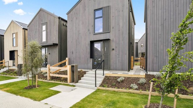 En modern bostadsbyggnad med ett platt tak, stora fönster och en välskött gräsmatta.