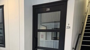 A black-framed door with the number 22B, a white wall, a white radiator, and a staircase with a handrail.