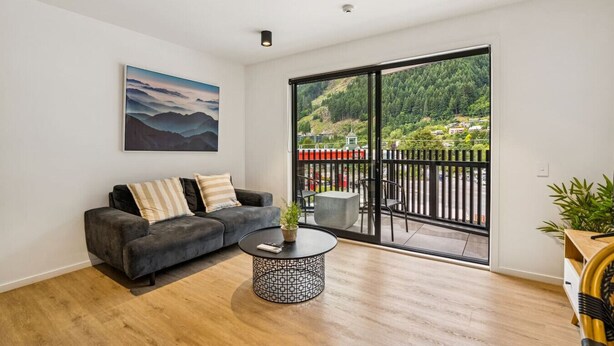 A modern living room with a grey sofa, a round coffee table, and a large window with a view of a forested hillside.
