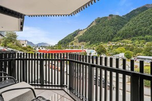 Un balcon avec vue sur une montagne, un bâtiment rouge et un parking.