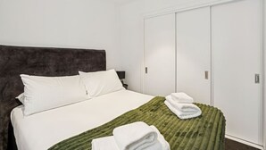A hotel room with a bed, a green textured blanket, white pillows, and a white wardrobe.